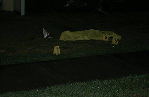 The body of Trayvon Martin covered with an emergency blanket in background. Crime scene markers identify various objects on the ground.
