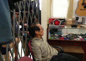 Minh Electronics owner sits  handcuffed inside store before being led away, July 25, 2013. (Photo: WONO)